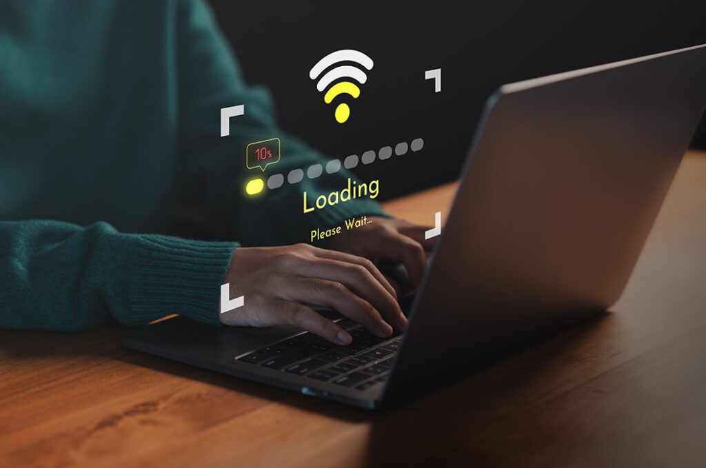 Person tippt konzentriert am grauen Laptop mit WLAN Ladeanzeige in Gelb.